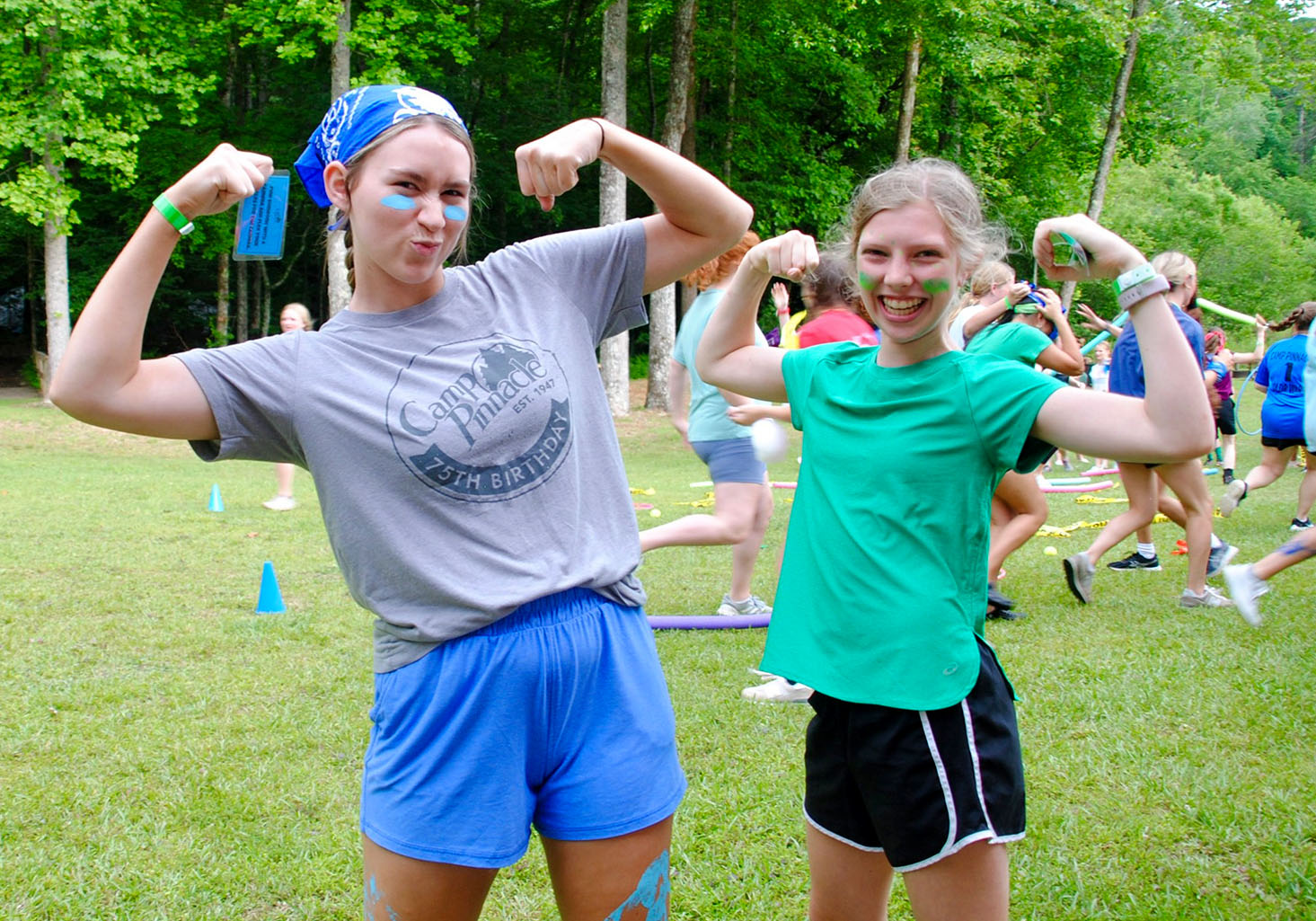 A college-age female camp staffer and a younger female camper pose with their arms flexed outside.